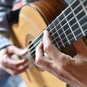 Nauaufnahme einer Person, die Gitarre spielt. Man sieht die Hände und die Gitarrenseiten.