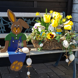 Osterhasenfigur aitz auf einer Bank neben einem Blumengesteck